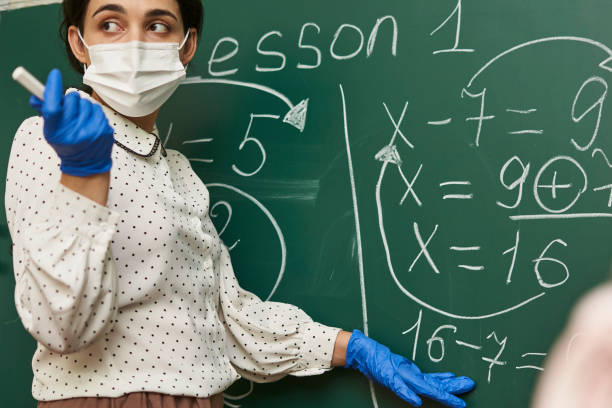 istock Fmale teacher wearing a facemask with latex gloves and explaining a math formula to the class 1464050962