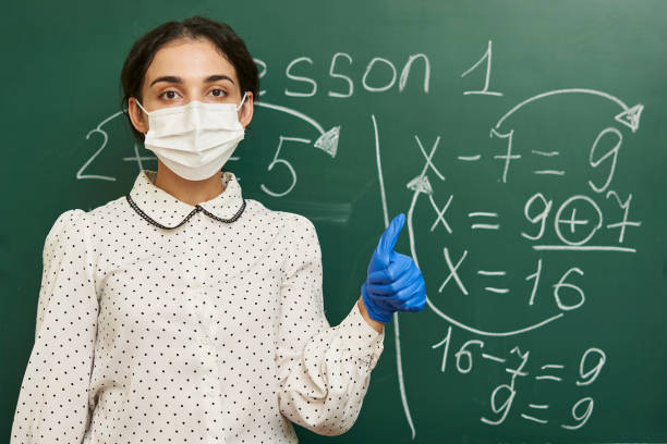 istock Female teacher wearing a facemask with latex gloves and explaining a math formula to the class 1464050984