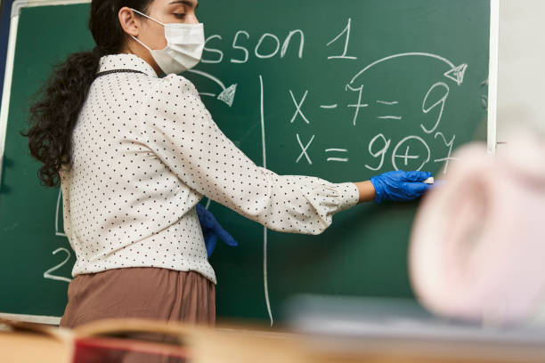istock Female teacher wearing a facemask with latex gloves and explaining a math formula to the class 1464050997