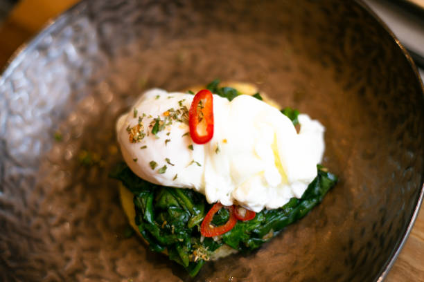 Mouthwatering selective focus shot of eggs Benedict with spinach and chili on a metal plate