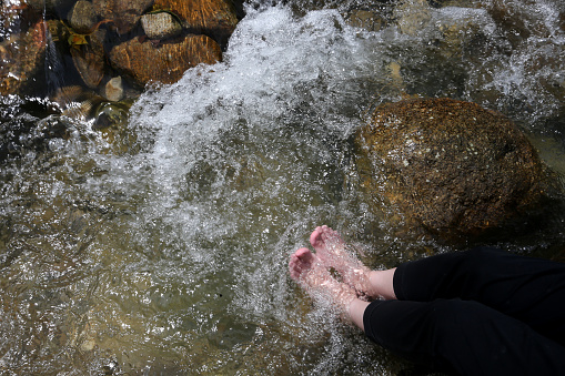 Human foot soaking in waterfall flowing water