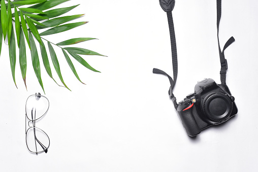 A top view of a camera, a pair of glasses and a tropical green leaf on an isolated background with copy space