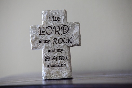 A soft focus of a carved rock cross with a printed bible verse