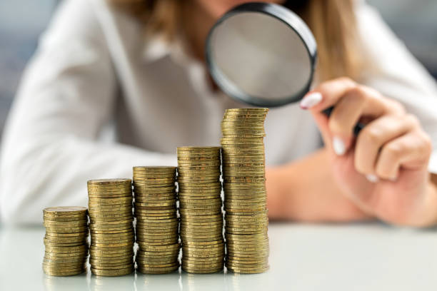 businesswoman looks at stacks of coins through a magnifying glass. - coin collection imagens e fotografias de stock