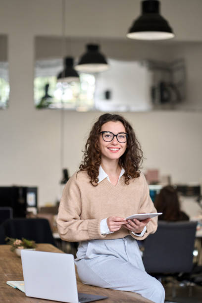 istock Young happy business woman holding tablet posing in office, vertical. 1464069355