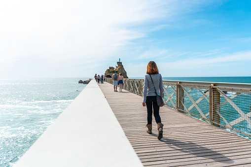 A young woman strolling along the wooden bridge in Plage du Port Vieux touristic beach in Biarritz municipality, France