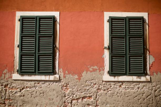 A beautiful textured facade in Venice with terracotta coloured paint and green window shutters.