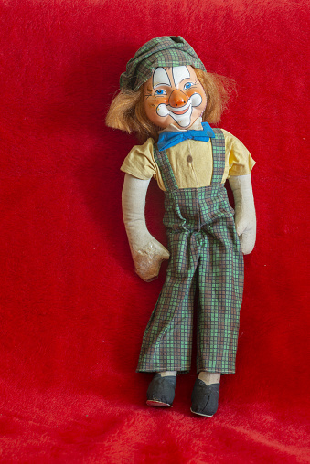 A vertical shot of a vintage clown doll on a red background