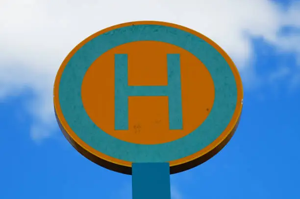 Tram and bus stops in Germany are marked with a green 'H' on a yellow background. Traffic sign no. 224. Against a blue-white sky in Frankfurt.