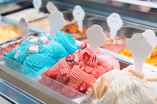 Summer sweet in italian gelateria. Close up of colourful delicious ice cream in trays in showcase fridge at confectionery shop. Price tag with mock up.