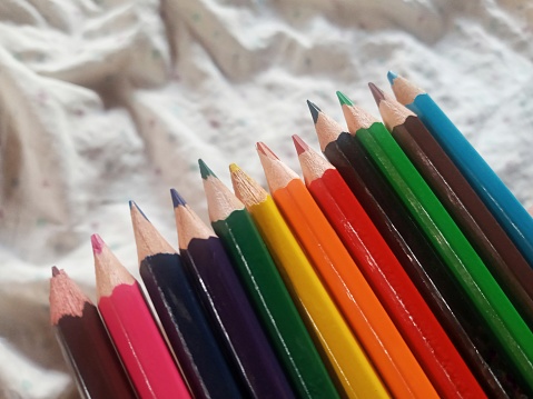 A line of coloring pencils on a white blurred fabric