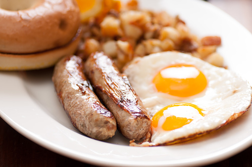 A closeup shot of eggs with English banger sausages on a white plate