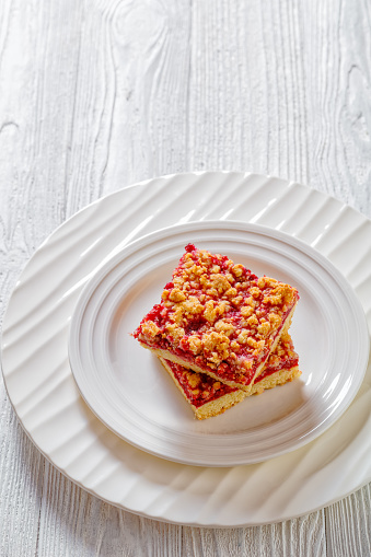 Raspberry Crumble Bars on white plate on white wood table, vertical view from above, free space