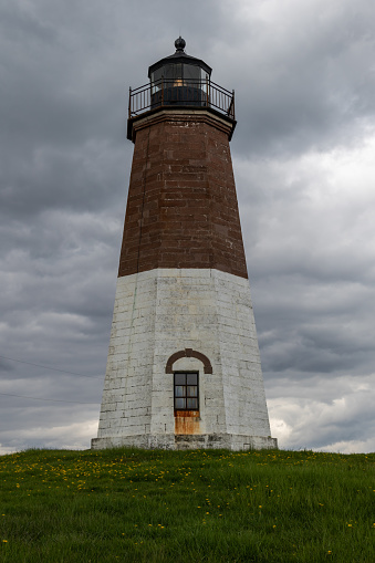 A vertical shot of the Point Judith Lighthouse in Narragansett, Rhode Island under a cloudy gray sky