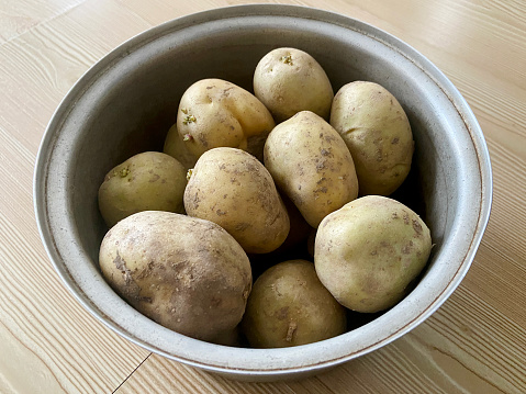 Fresh raw potatoes in a pot on the wood background