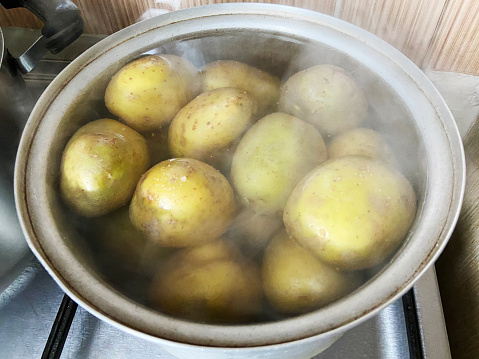 Potatoes cooking in a pot on the cooker with steam, boiling raw potatoes
