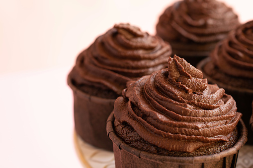 Close-up of chocolate cupcakes with chocolate frosting on pink background.