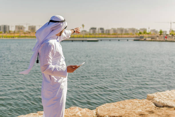 Islamic man, in traditional clothes, working with a tablet at a maritime site. An Islamic man, in traditional clothes, working with a tablet at a maritime site. kaffiyeh stock pictures, royalty-free photos & images
