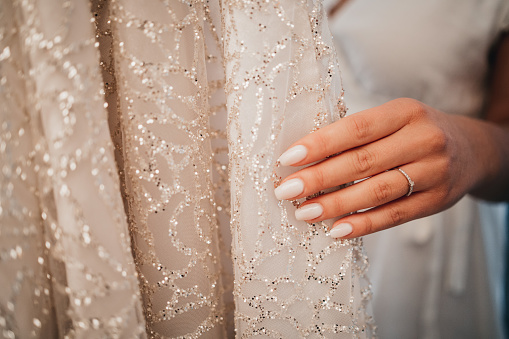A closeup shot of the bride's hand with a ring on it touching her gorgeous wedding dress