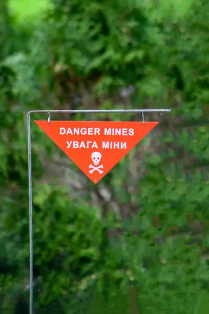 Danger mines. Sapper minefield warning sign on green background. Jolly Roger - white skull crossbones on a red sign of the danger of landmines. Military mine. War in Ukraine. Ukrainian translation