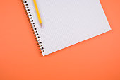 Grid notebook and a pencil isolated on orange background with free space for text
