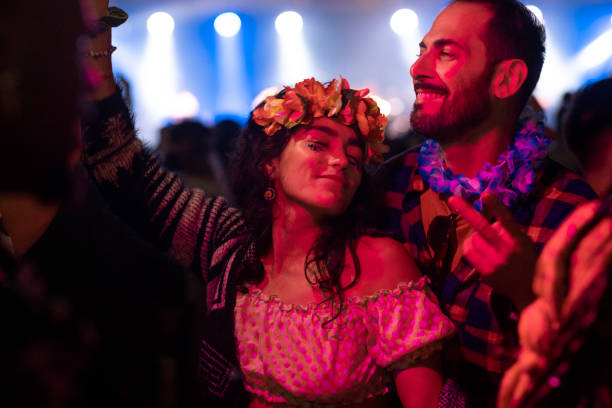 A couple dancing together at a night festival and having a good time. They are happy and smiling and sharing positive energy. The woman is wearing a floral crown on her head.