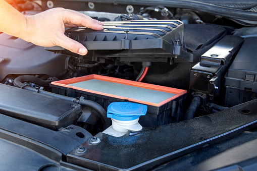 Replacing an old dirty air filter in the engine compartment of a car engine. The mechanic is servicing the car. Cleaning the air in the car engine.