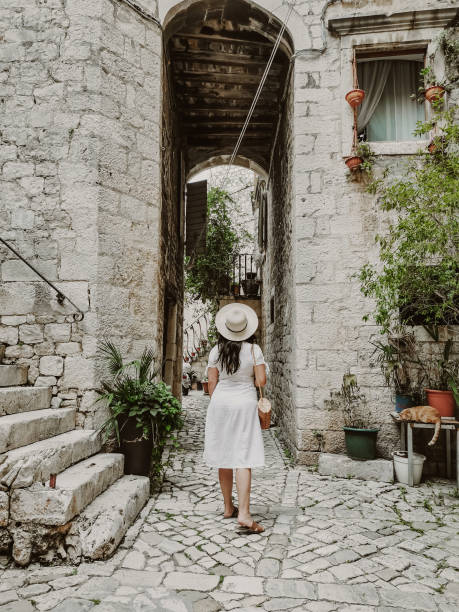 vista posteriore della donna che indossa vestito bianco che cammina nell'idilliaca vecchia strada nella città di trogir, croazia. - traù foto e immagini stock