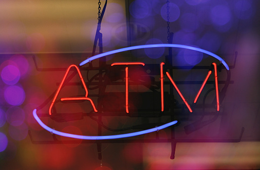 A bright neon illuminated ATM sign on a bokeh light background