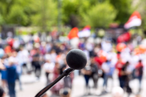 istock Protest, public demonstration or pension reform strike, focus on microphone, blurred crowd of people in the background 1464104826
