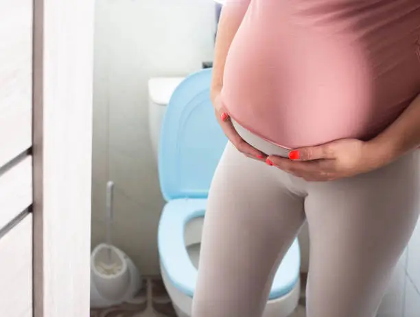 Photo of Pregnant girl with a big belly on the background of the toilet. The concept of frequent urination in pregnant women. Copy space for text