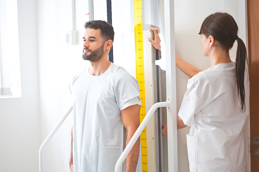 Female healthcare expert measuring height of male patient in hospital