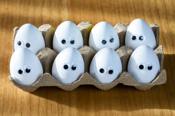 Funny faces on white eggs in carton box with organic chicken eggs on kitchen table closeup big animation eyes. humor, food and easter holiday concept. close up