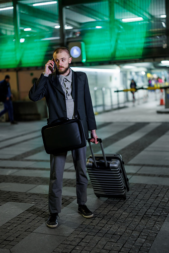 The image shows a young businessman exiting an airport carrying a suitcase and talking on the phone at the same time.
