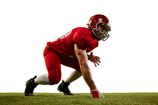 At start. Dynamic portrait of american football player in sports uniform and protective helmet training on grass flooring isolated over white background. Sport, team, competition, championship