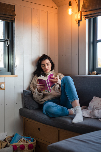 Woman relaxing while on staycation at a cabin in the North East of England. She is sitting reading a book, having time to herself.