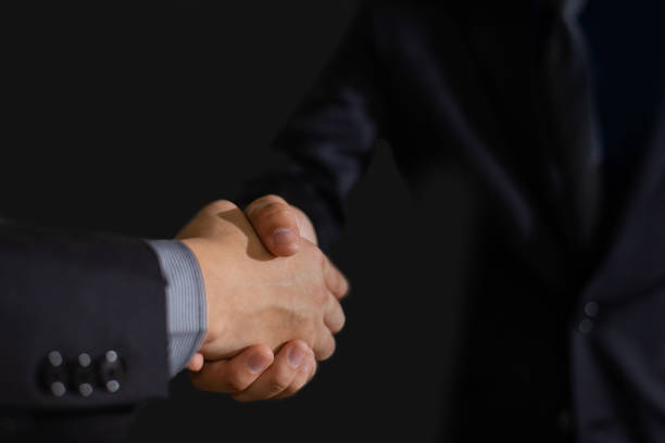 istock Handshake with hands clasped against a dark background 1464116686