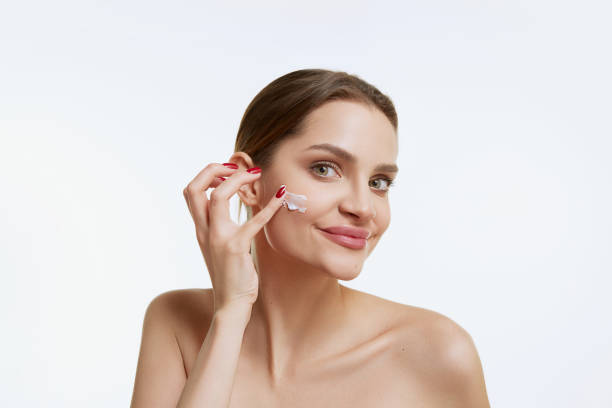 istock Young beautiful girl with smooth clear face applying face moisturizing cream, posing over grey background. Concept of natural beauty, cosmetology 1464120180