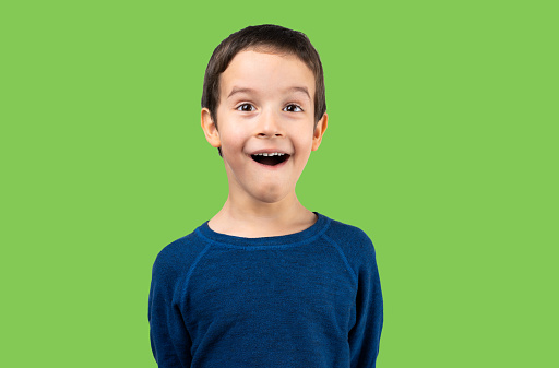 Dark haired little child making listen gesture with shocked face, looking skeptical and sarcastic, surprised with open mouth isolated on green
