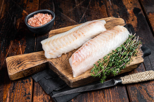 istock Cod fish fillets, raw codfish with thyme on wooden board. Wooden background. Top view 1464120805