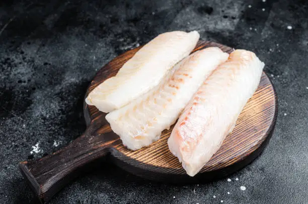 Fillets of codfish, raw cod fish meat. Black background. Top view.