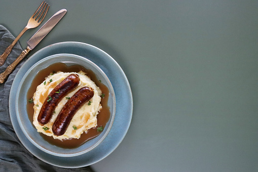 Stock photo showing elevated view of homemade bangers and mash with rich onion gravy covering sausages and mashed potato.