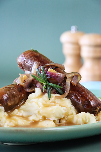 Stock photo showing close-up view of hearty comfort food of homemade bangers and mash with rich onion gravy covering sausages and mashed potato served with garden peas.