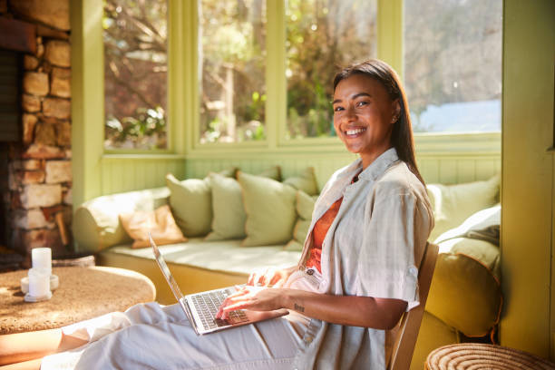 istock Young woman smiling while using a laptop on a chair at home 1464121676