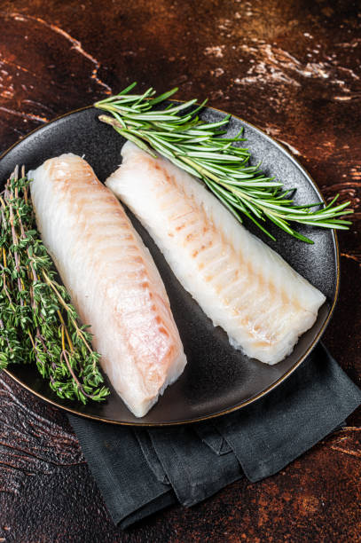 istock Raw cod loin fillet steaks with herbs on plate. Dark background. Top view 1464122368