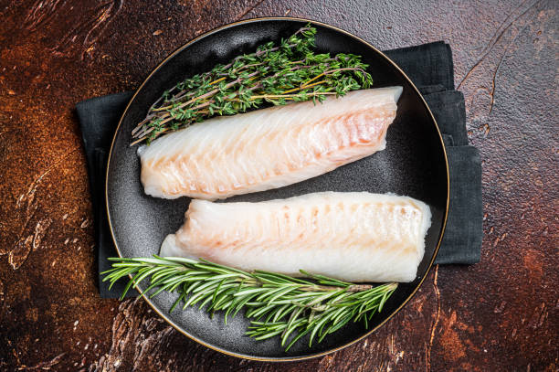 istock Raw cod loin fillet steaks with herbs on plate. Dark background. Top view 1464122393