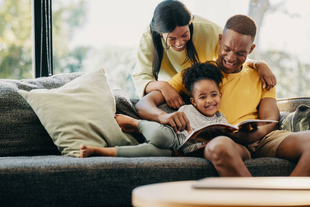 niña feliz leyendo un cuento con su mamá y su papá - child reading mother book fotografías e imágenes de stock