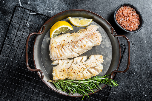 High angle view of various fresh fish and seafood decorated with ice cubes, lemon slices, herbs and vegetables on blue wooden background