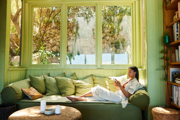 Young woman sitting on her sofa and texting on her phone - fotografia de stock