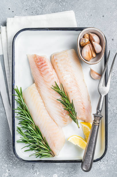 istock Uncooked Raw cod loin fillet steaks with herbs in kitchen tray. Gray background. Top view 1464124730